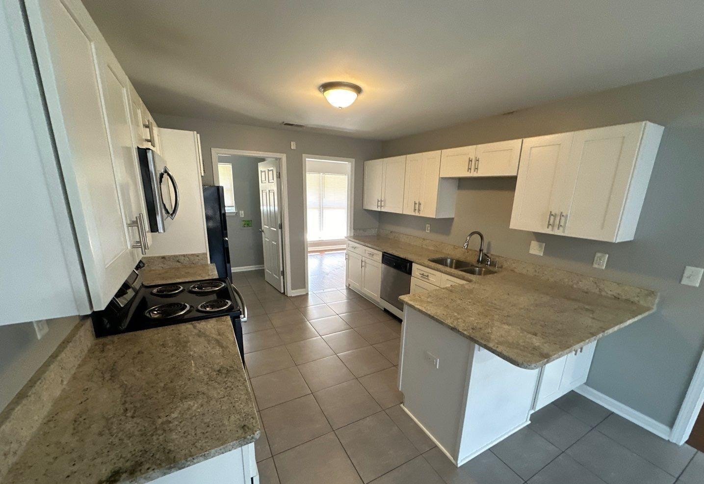 9420 Grove Road Cordova, TN 38016 - Photo 6 of 15 Kitchen with white cabinetry, a peninsula, black appliances, dark tile patterned floors, and light stone countertops