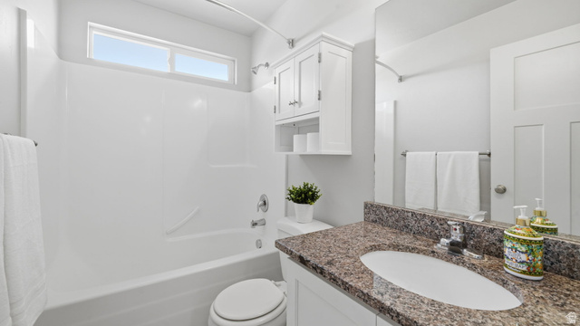 111 East Silver Oak Road Vineyard, UT 84059 - Photo 28 of 50 Bathroom featuring a white bathtub with an overhead transom window, a white toilet, and a vanity with a granite-style countertop, undermount sink, and white cabinetry