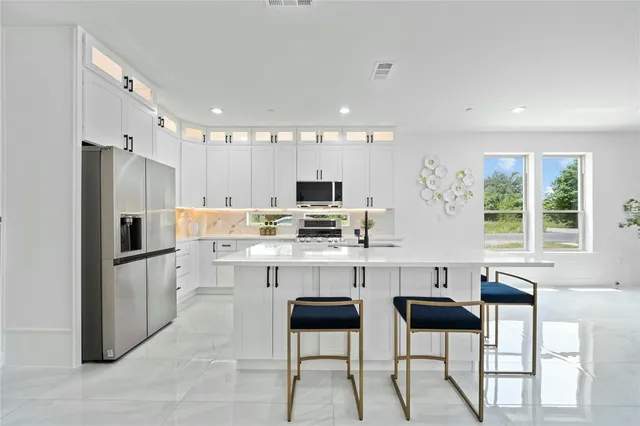 a kitchen with stainless steel appliances kitchen island granite countertop a refrigerator and a stove top oven with white cabinets
