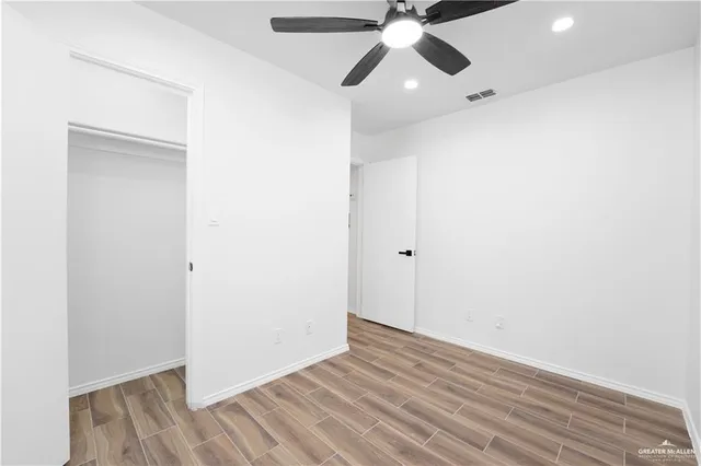 an empty room with wooden floor fan and windows