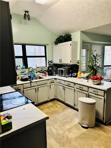 a kitchen with a sink dishwasher stove and white cabinets next to a window