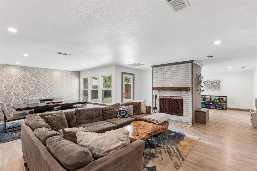 5216 Ashbrook Road Dallas, TX 75227 - Photo 7 of 28 Spacious great room showcasing a sectional layout anchored by wide-plank wood-finish flooring, recessed ceiling lighting, and a striking brick fireplace with wood mantel