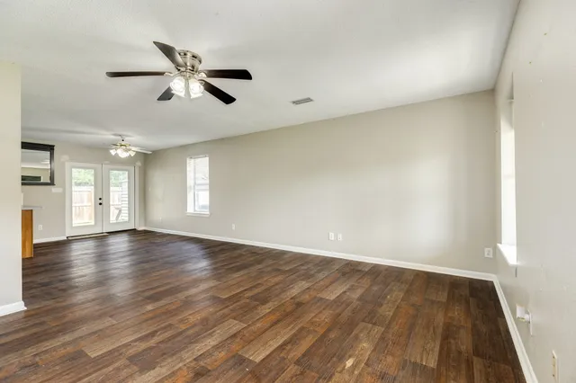 an empty room with wooden floor fan and windows