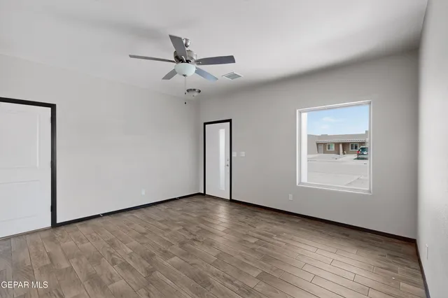 an empty room with wooden floor chandelier fan and windows