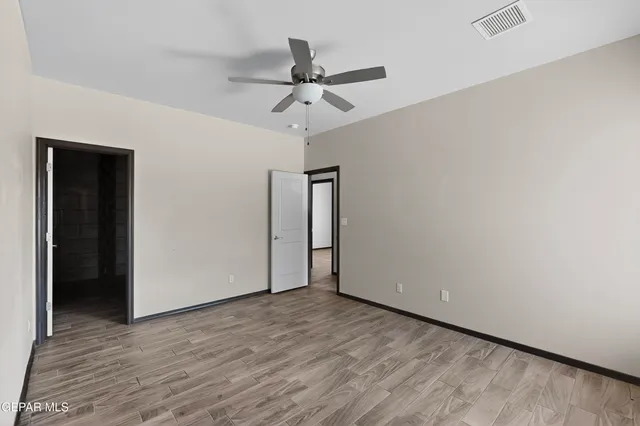 a view of an empty room with wooden floor and a ceiling fan