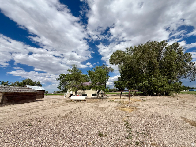 2865 North 3250 W Road Sutherland, UT 84624 - Photo 25 of 28 Expansive gravel lot featuring a large outbuilding with a metal roof, a white residential structure with exterior stairs, and multiple mature trees