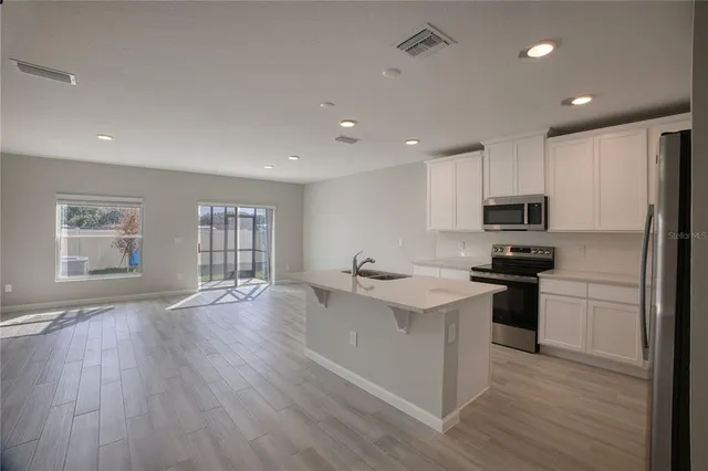 a kitchen with stainless steel appliances granite countertop a refrigerator a sink dishwasher a stove and white countertops with wooden floor