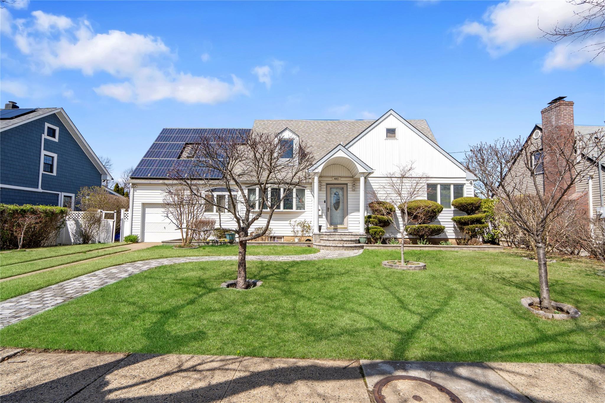 Cape cod house with an attached garage, solar panels, and a front lawn
