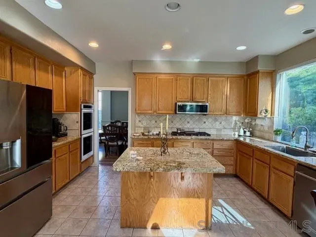 a large kitchen with kitchen island granite countertop wooden cabinets a sink a stove a refrigerator and blue cabinets