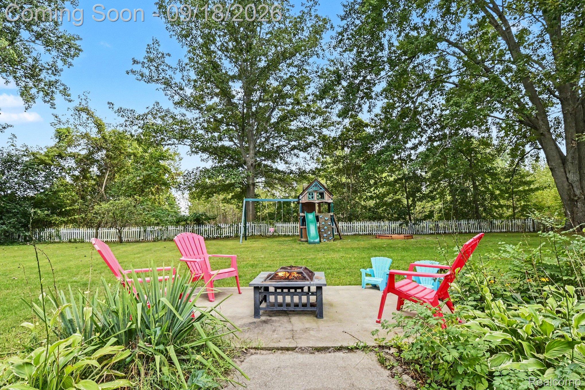 Expansive green lawn with mature trees, a concrete patio, and a white picket fence