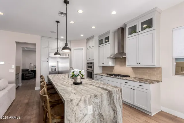 a kitchen with granite countertop a stove a sink a refrigerator and white cabinets with wooden floor