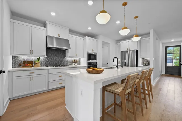 a kitchen with stainless steel appliances kitchen island granite countertop a sink a stove white cabinets and wooden floor