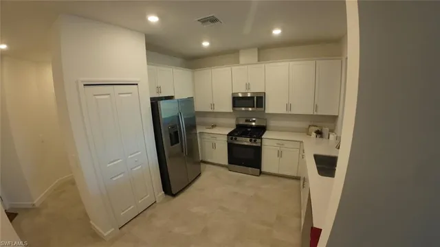 a kitchen with stainless steel appliances a refrigerator a sink and white cabinets