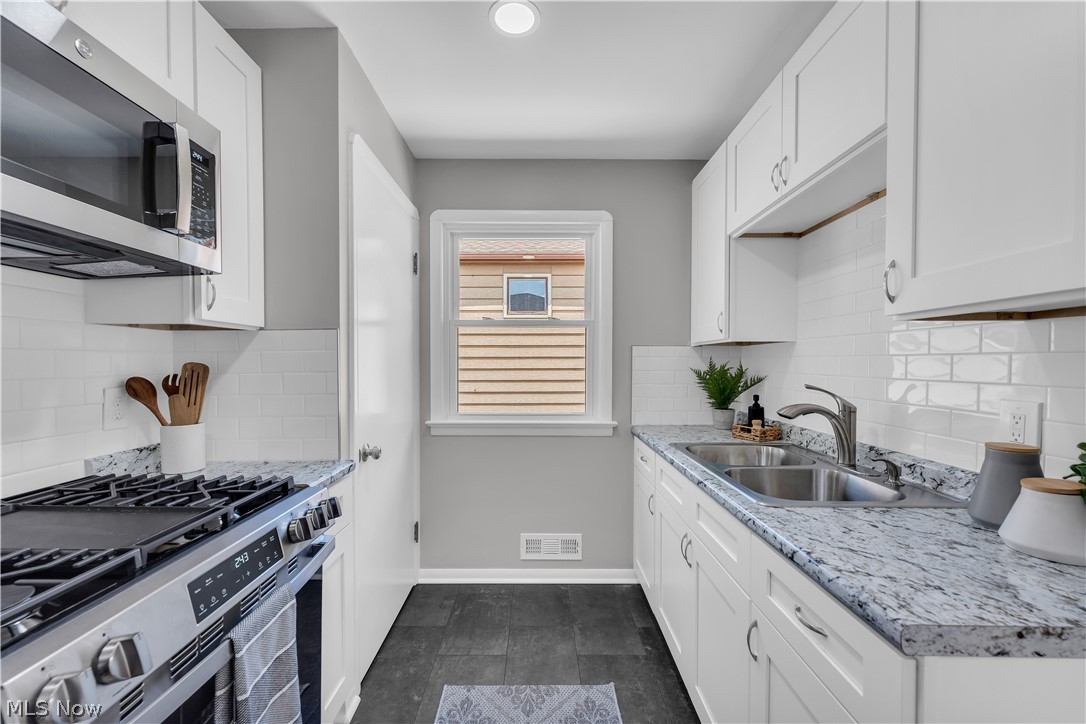 4322 Roadoan Road Brooklyn, OH 44144 - Photo 13 of 27 Kitchen with appliances with stainless steel finishes, white cabinets, dark tile patterned floors, and decorative backsplash