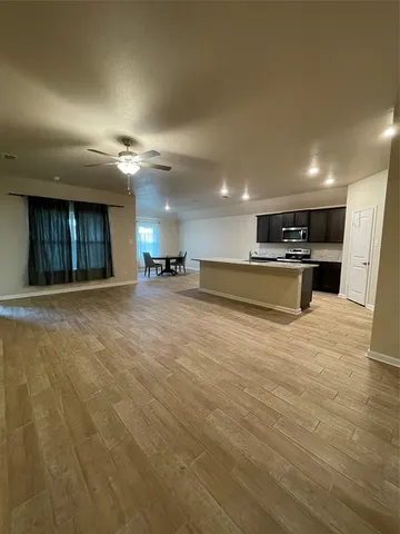 a large kitchen with stainless steel appliances a large counter top a stove and a refrigerator with wooden floor