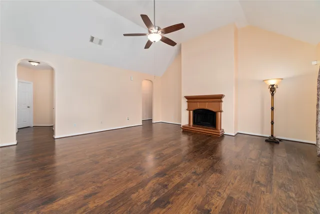 an empty room with wooden floor a ceiling fan a fireplace and windows