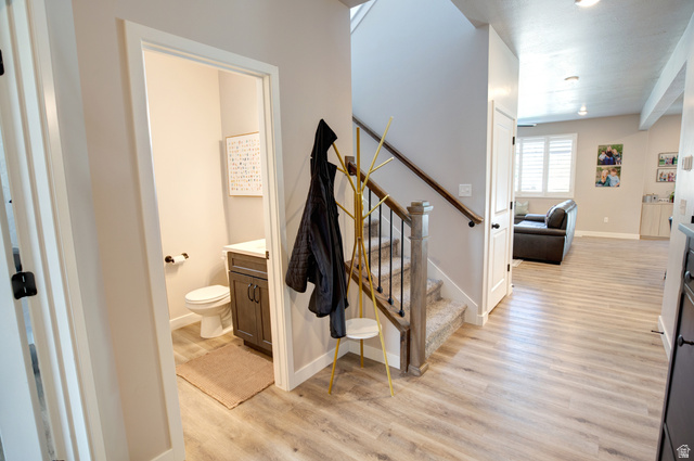 983 South 950 West Provo, UT 84601 - Photo 22 of 56 Entryway featuring light wood-finish flooring, a carpeted staircase with wood newel posts and handrail, and an adjacent powder room with a dark wood vanity and white countertop
