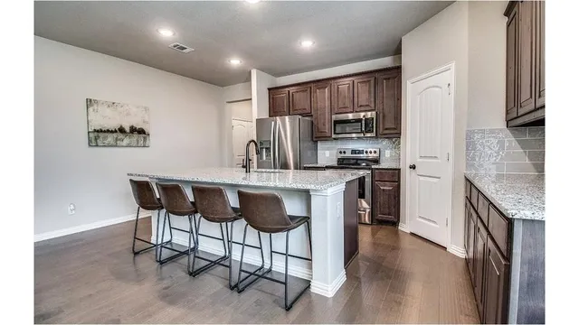 a kitchen with stainless steel appliances granite countertop a stove top oven a sink a refrigerator and a dining table with wooden floor