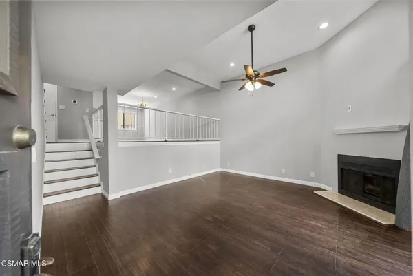 an empty room with wooden floor a ceiling fan a fireplace and windows