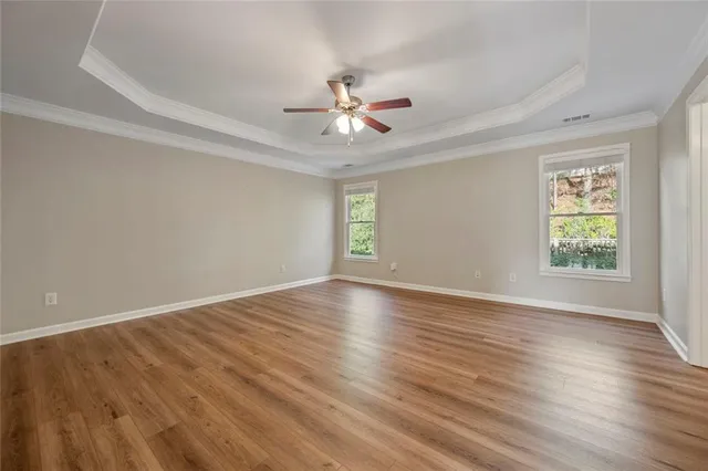 an empty room with wooden floor chandelier fan and windows