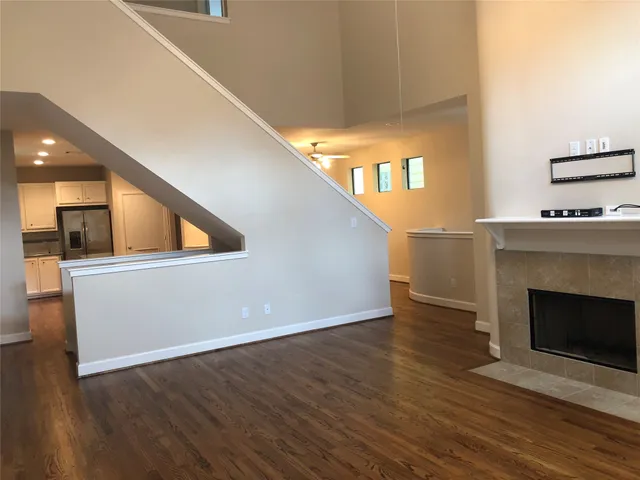 a view of an empty room with wooden floor and a kitchen