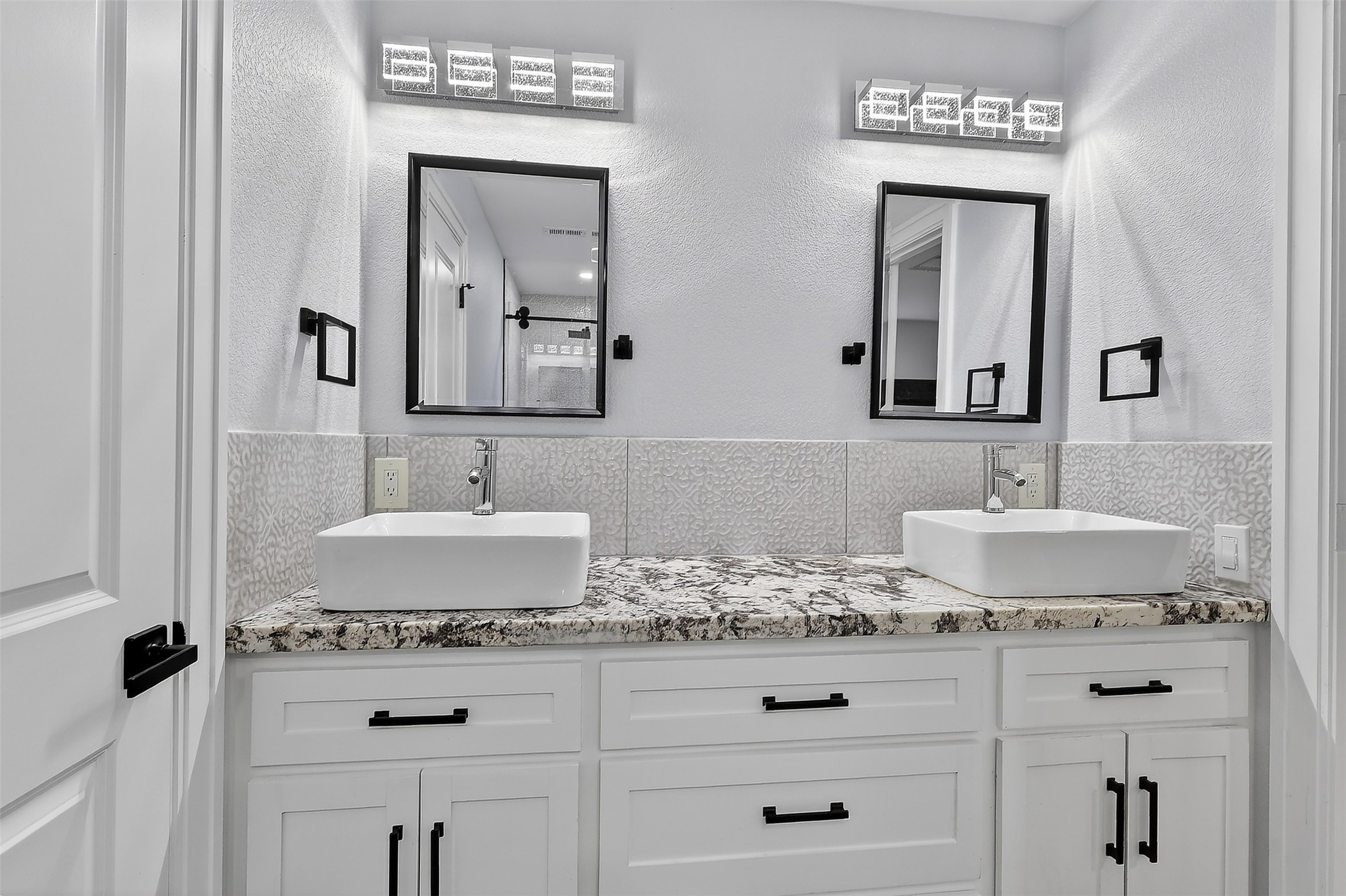 17106 Spring Creek Forest Drive Spring, TX 77379 - Photo 28 of 49 A unique, patterned backsplash runs behind the sinks, adding a subtle layer of sophistication to the neutral color palette.
