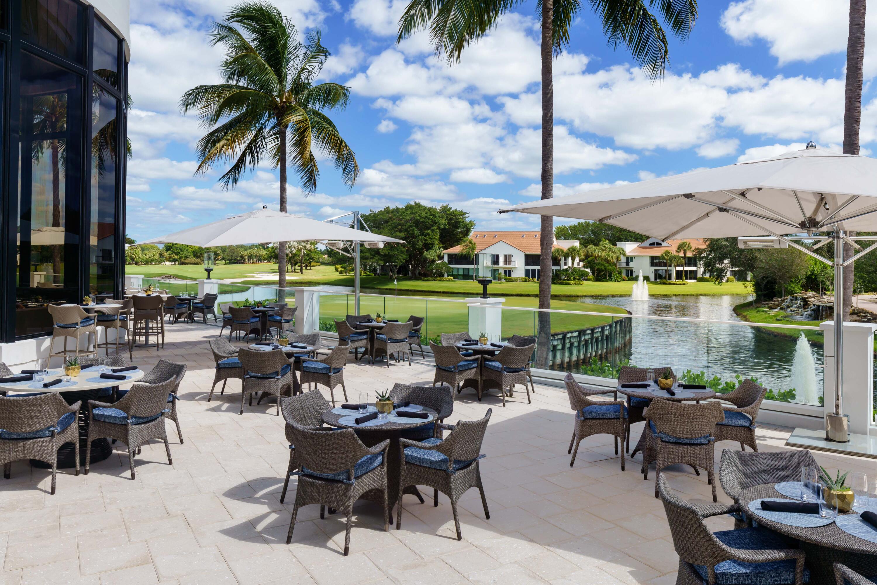 5887 Northwest 24th Avenue, Unit 1203 Boca Raton, FL 33496 - Photo 46 of 62 a view of a patio with couches table and chairs under an umbrella with palm trees