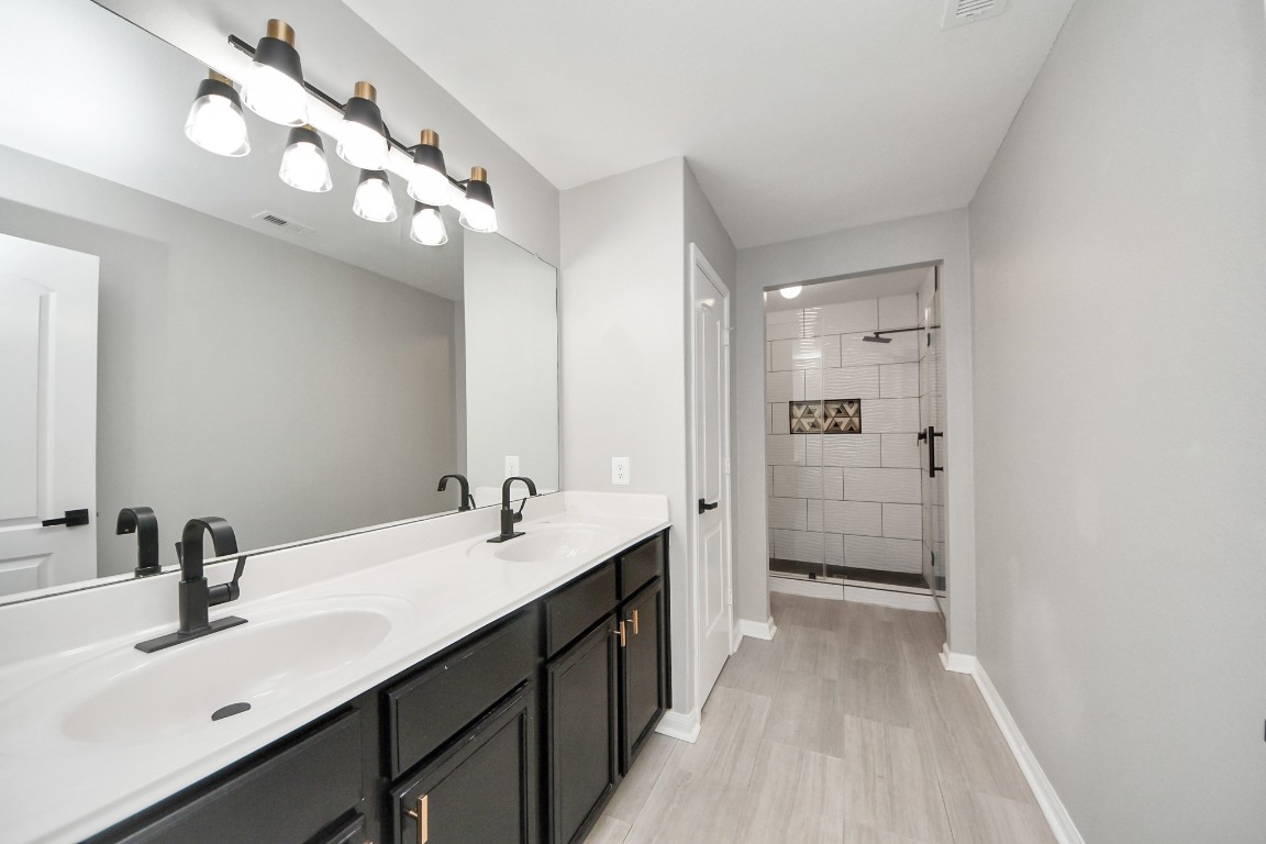 6931 Primrose Road Baytown, TX 77521 - Photo 36 of 50 Stylish upstairs bathroom featuring a dual-sink vanity with modern black fixtures, a large mirror, and a beautifully tiled walk-in shower with decorative accents.