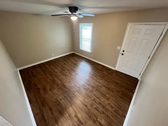 an empty room with wooden floor fan and windows