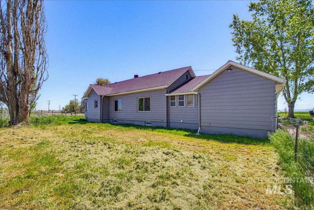 30013 Apple Valley Road Parma, ID 83660 - Photo 24 of 25 Ranch-style residence featuring light gray siding, multiple windows, a dark roof, and mature trees on the property boundary