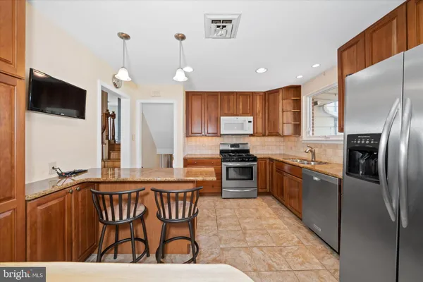 a kitchen with stainless steel appliances granite countertop a refrigerator a stove a sink a dining table and chairs with wooden floor