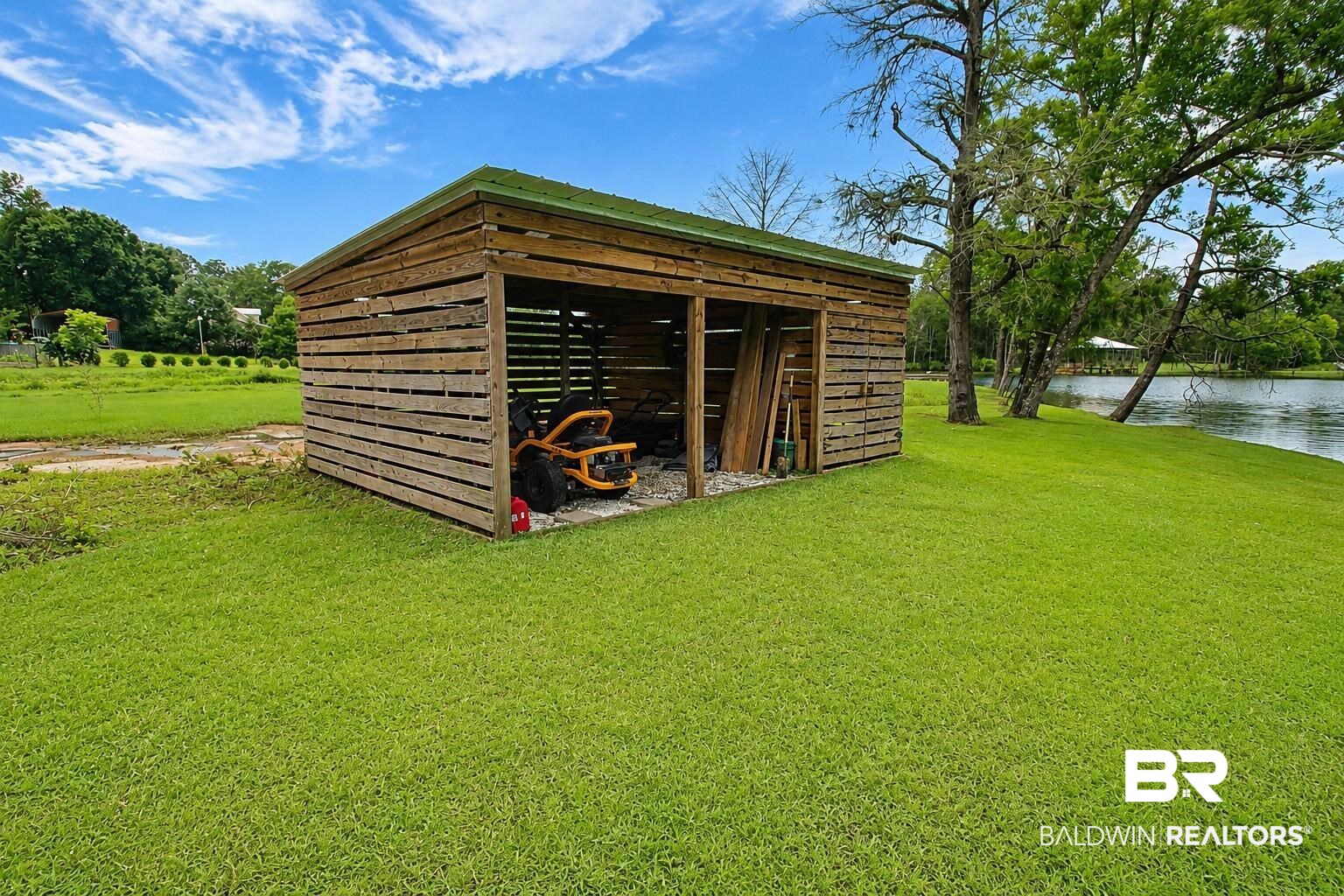 9825 Wolf Creek Ridge Elberta, AL 36530 - Photo 66 of 76 Wood-sided outbuilding with a green metal roof, featuring open-air storage bays, a gravel floor, and a grassy surround