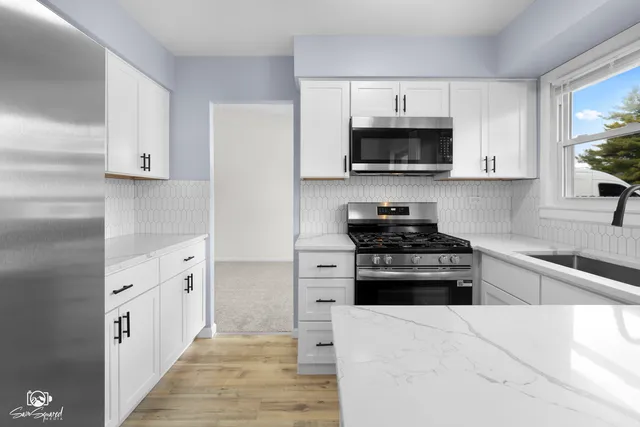 a kitchen with stainless steel appliances granite countertop white cabinets a stove a microwave and a refrigerator