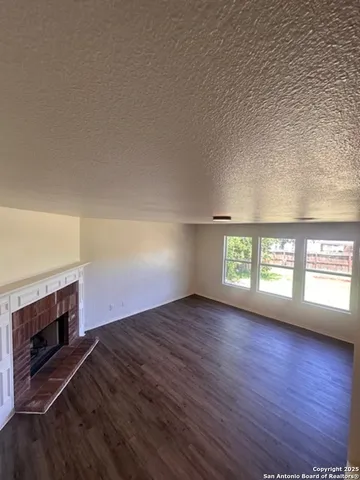 an empty room with wooden floor fireplace and windows