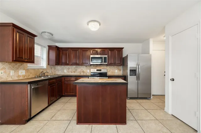 a kitchen with stainless steel appliances granite countertop a stove top oven a sink dishwasher and a refrigerator with wooden cabinets