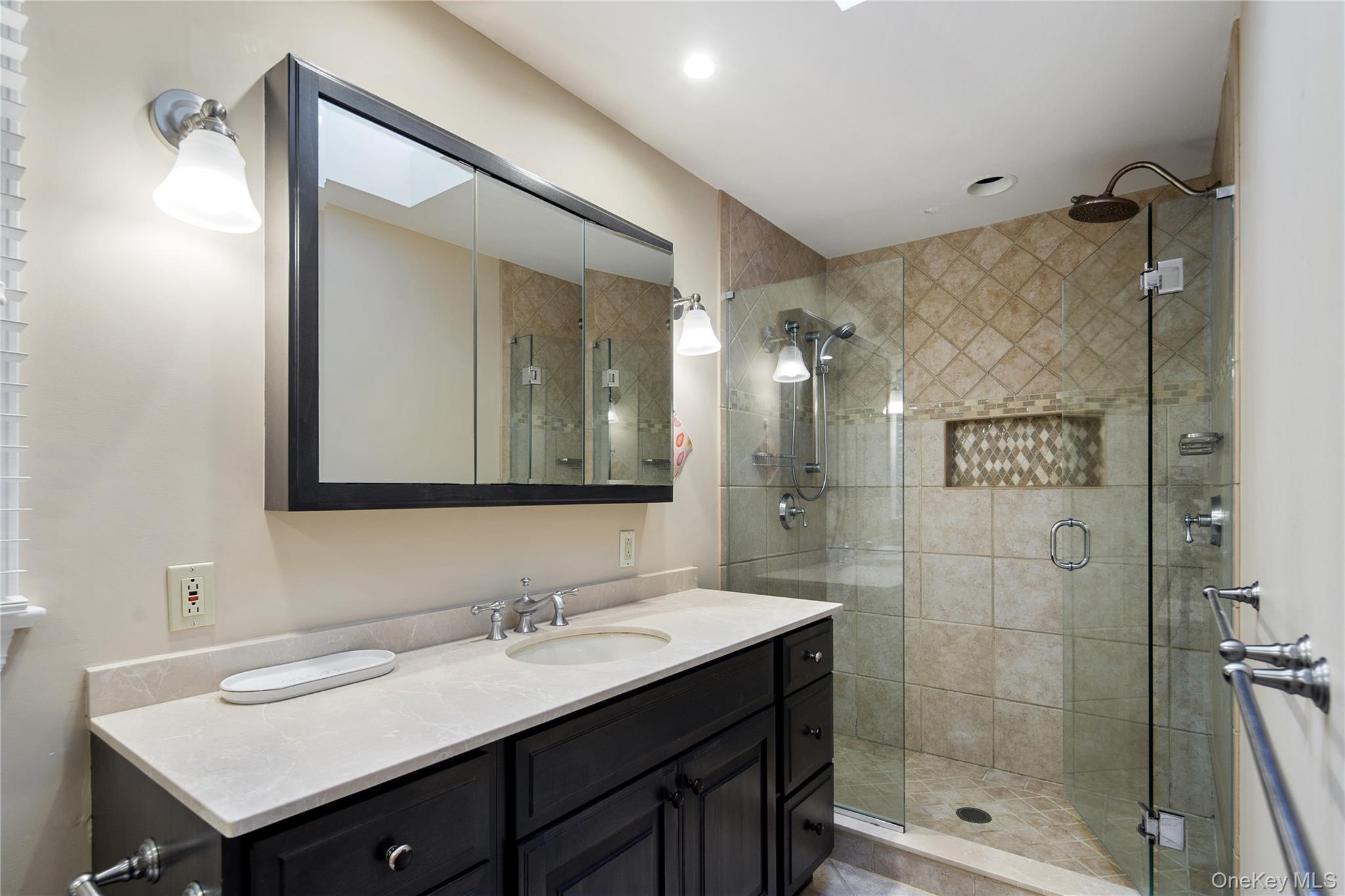 105 Cross Ridge Road Chappaqua, NY 10514 - Photo 30 of 43 The primary en-suite bath offers a large shower with frameless glass enclosure, rain head and adjustable shower heads, built-in product niche, large storage vanity with undermount sink, triple medicine cabinet with beveled edge mirrors, wall sconces, polished chrome plumbing fixtures and a separate jetted tub