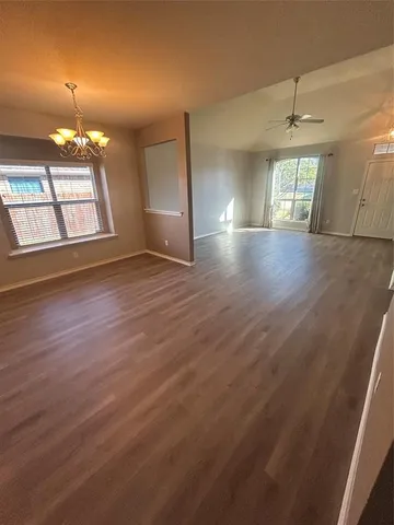 an empty room with wooden floor chandelier and windows