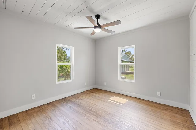 an empty room with wooden floor ceiling fan and windows