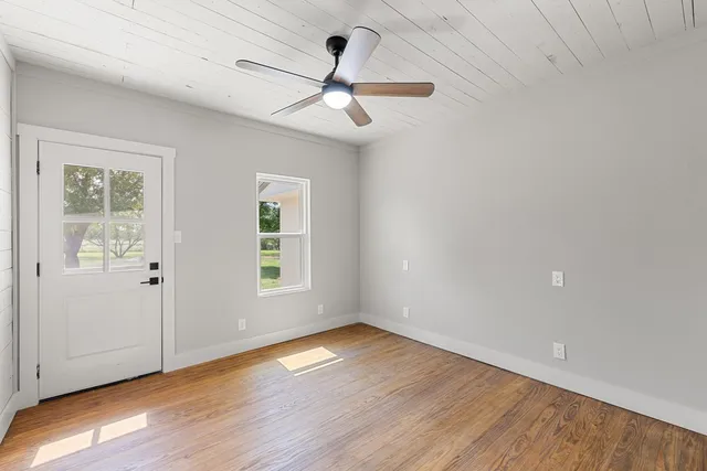 an empty room with wooden floor chandelier fan and windows
