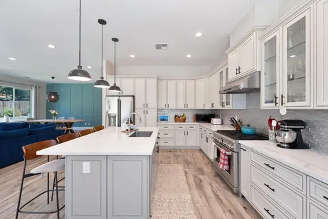 a kitchen with stainless steel appliances kitchen island granite countertop a refrigerator a sink dishwasher a stove and white cabinets with wooden floor