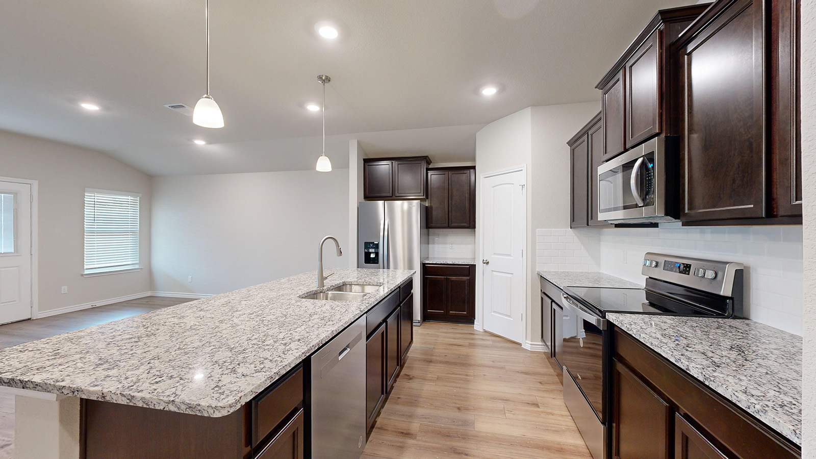 243 Water Wl Road Burnet, TX 78611 - Photo 4 of 23 Kitchen featuring an expansive island with a double basin sink, light-toned granite countertops, dark wood-finish cabinetry, and stainless steel appliances including a microwave, dishwasher, and range