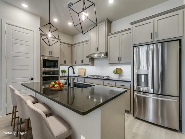 a kitchen with stainless steel appliances granite countertop a refrigerator a oven a sink a stove a dining table and chairs with wooden floor