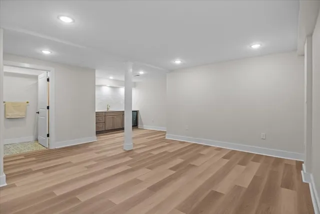 a view of an empty room with wooden floor and a kitchen