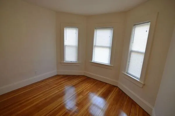 a view of an empty room with wooden floor and window