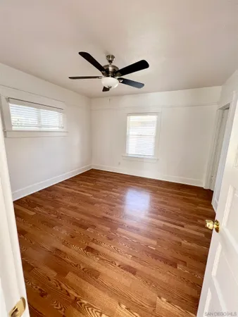 an empty room with wooden floor fan and windows