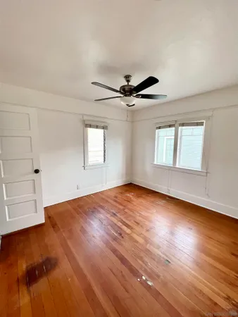 an empty room with wooden floor chandelier fan and windows