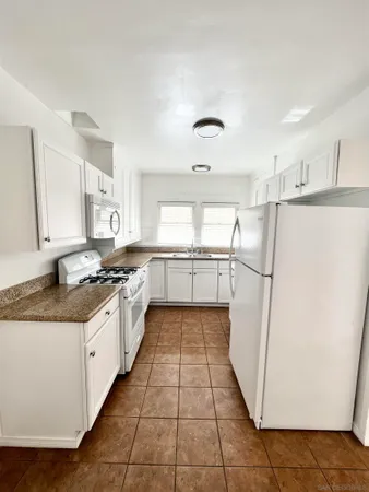 a kitchen with granite countertop a refrigerator a sink and white cabinets