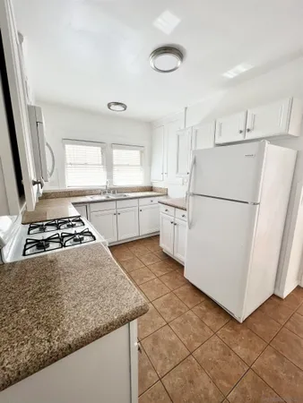 a kitchen with granite countertop a refrigerator sink stove and white cabinets