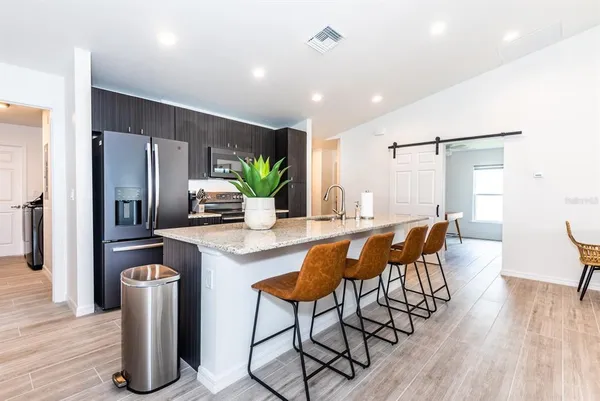 a kitchen with stainless steel appliances granite countertop a refrigerator a sink a stove a dining table and chairs with wooden floor