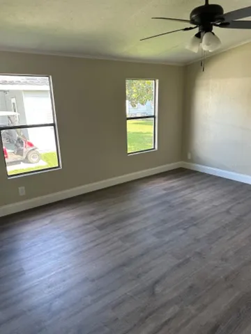 an empty room with wooden floor fan and windows